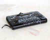 Black wallet with white text and designs on a light marble background