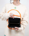 Person wearing a cream sweater with orange and green design, holding an open black wallet.
