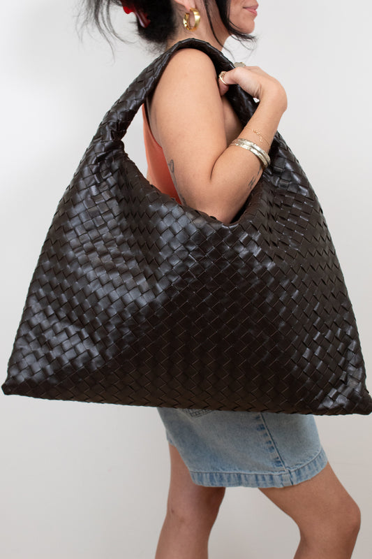 Woman holding a woven brown oversized  bag against a plain background