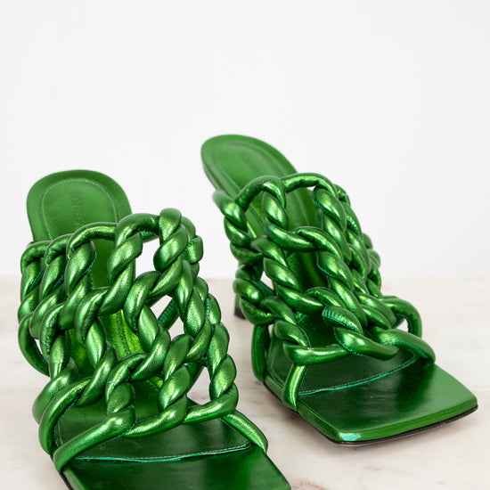 Pair of green metallic sandals with braided straps on a light background