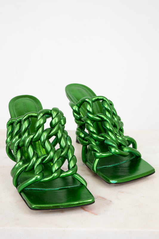 Pair of green metallic sandals with braided straps on a light background