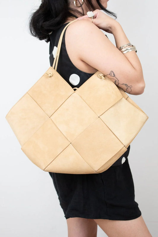 Beige quilted handbag held by a person against a white background
