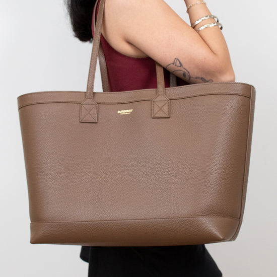 Person holding brown leather tote on white background