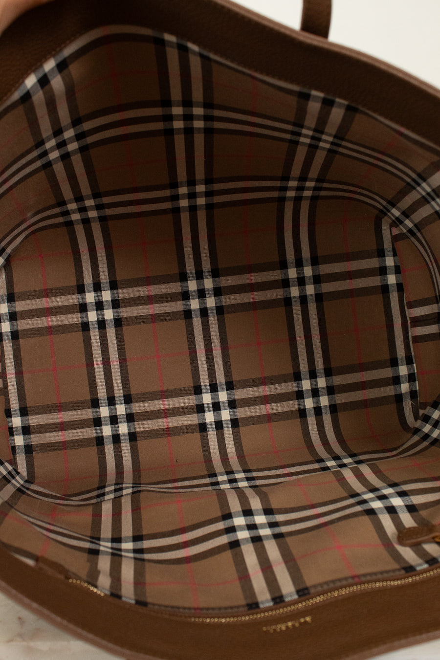 Close-up of a brown leather bag with plaid pattern on a light background