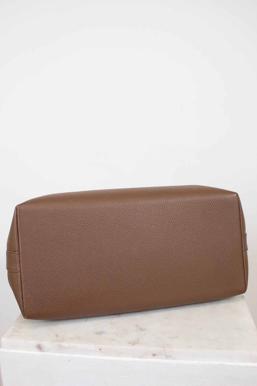 Brown leather bag on a white surface with a light gray background