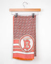 Coral and white patterned scarf with a logo on a hanger against a white background