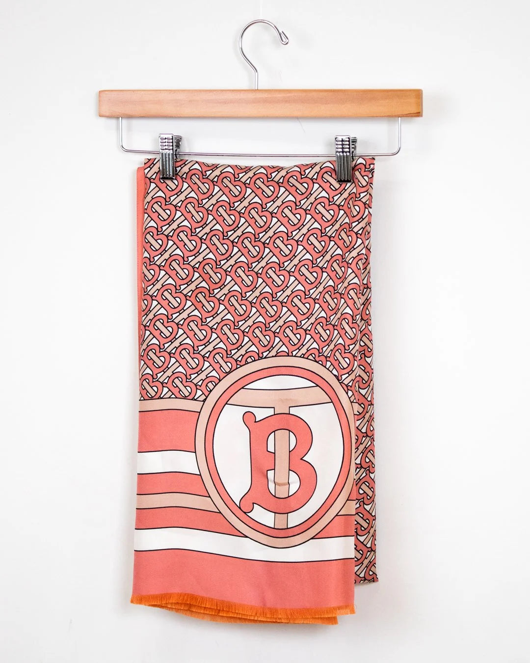 Coral and white patterned scarf with a logo on a hanger against a white background
