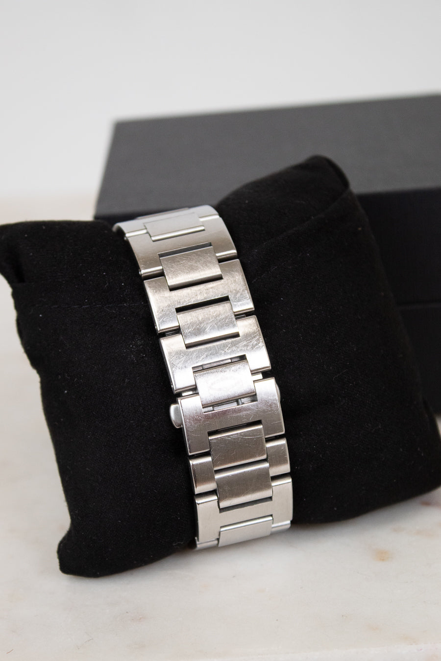 Silver watch band on a black cushion with a white background