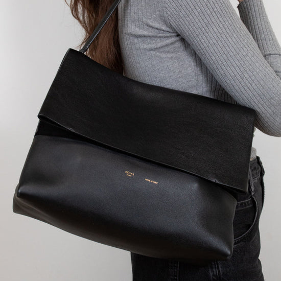 Person wearing a black leather shoulder bag against a plain background
