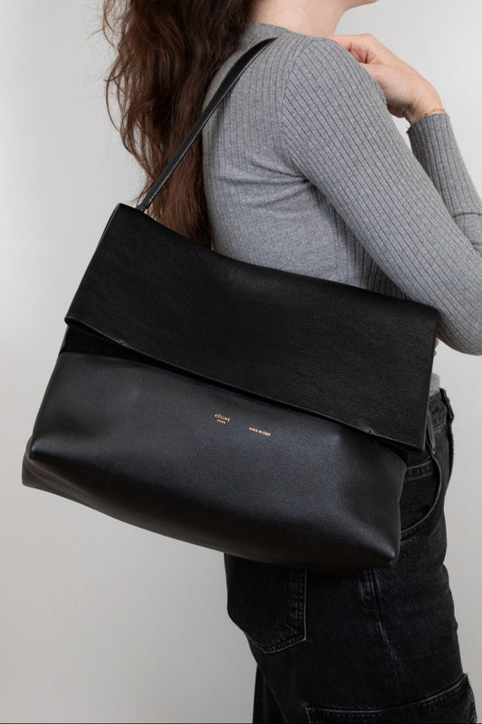 Person wearing a black leather shoulder bag against a plain background