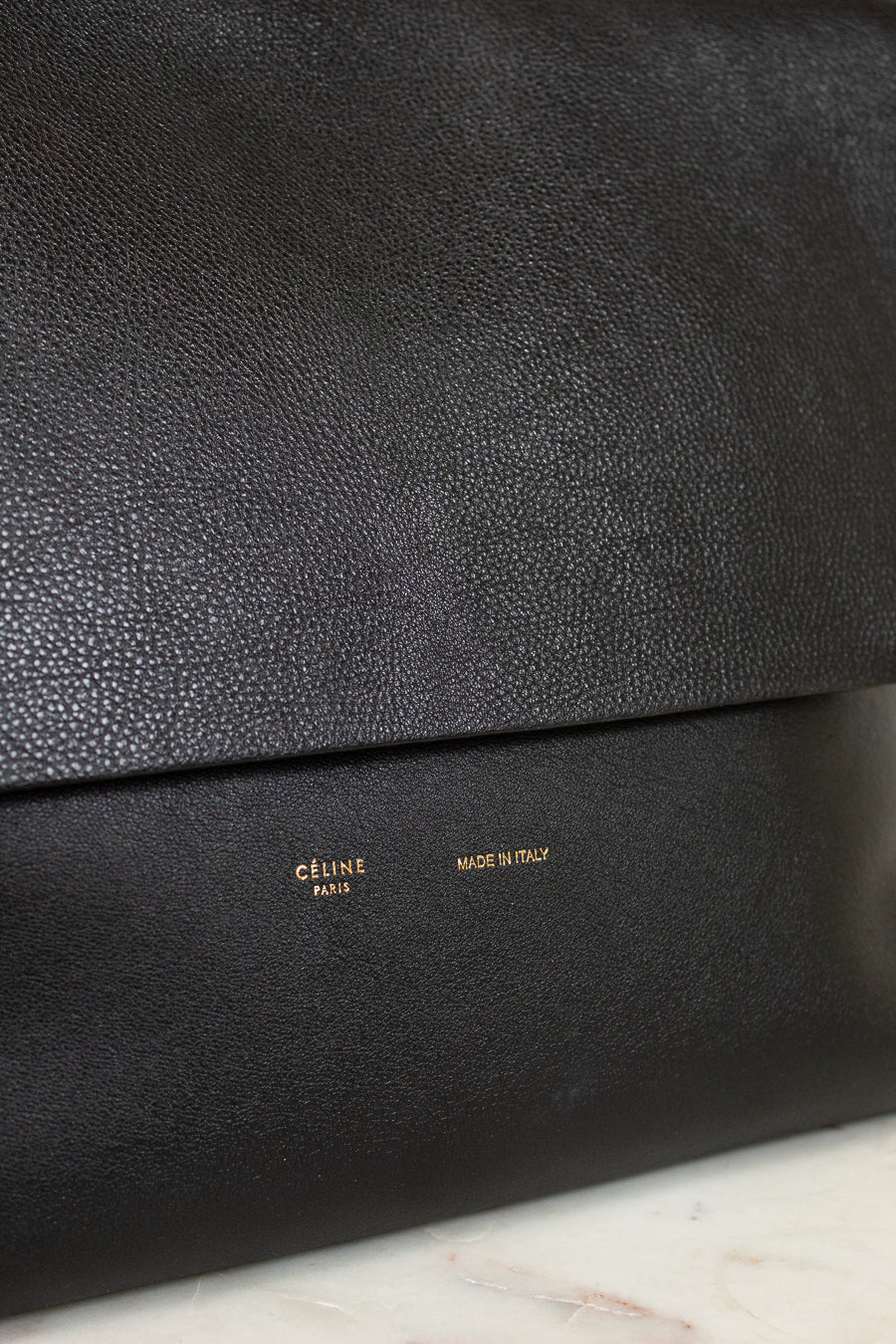 Close-up of a black leather clutch bag with 'Celine' branding on a marble surface.