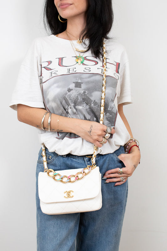 Person wearing a graphic t-shirt and jeans, holding a white handbag with gold chain strap.