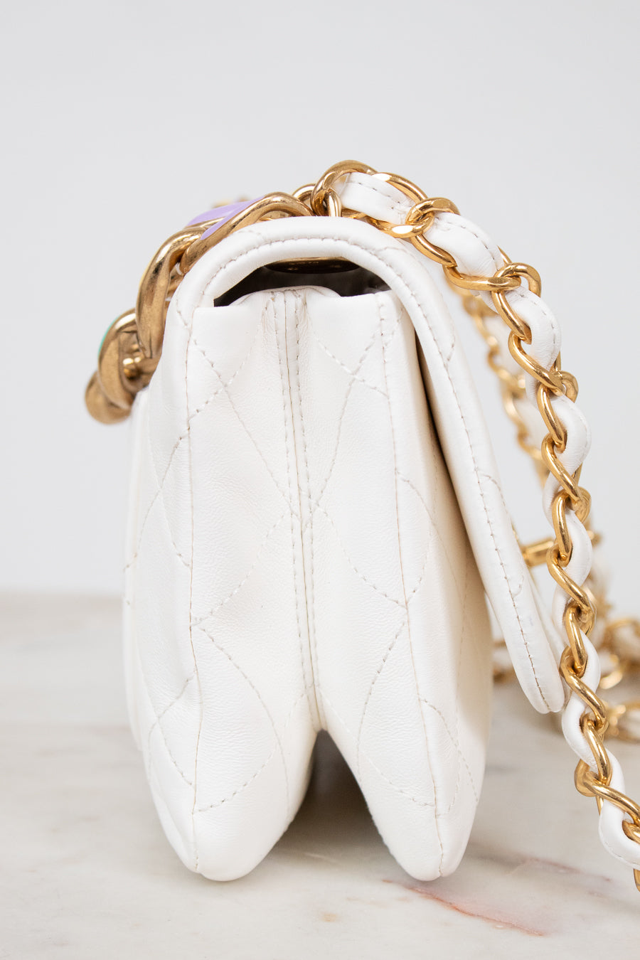 Side view of white quilted handbag with gold chain strap on a light gray background