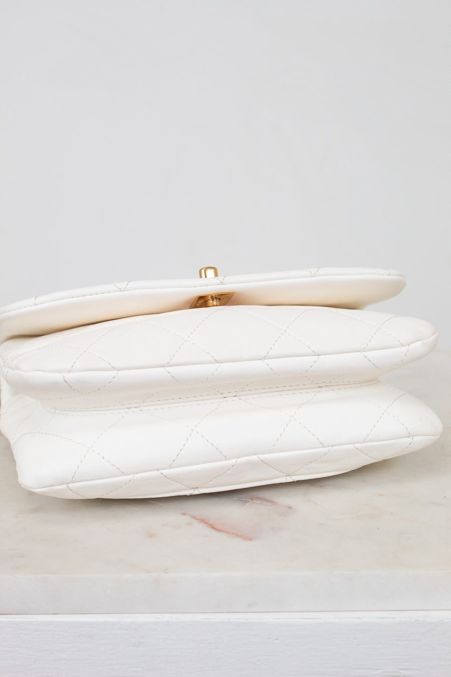 White clutch bag with gold clasp on a light gray background