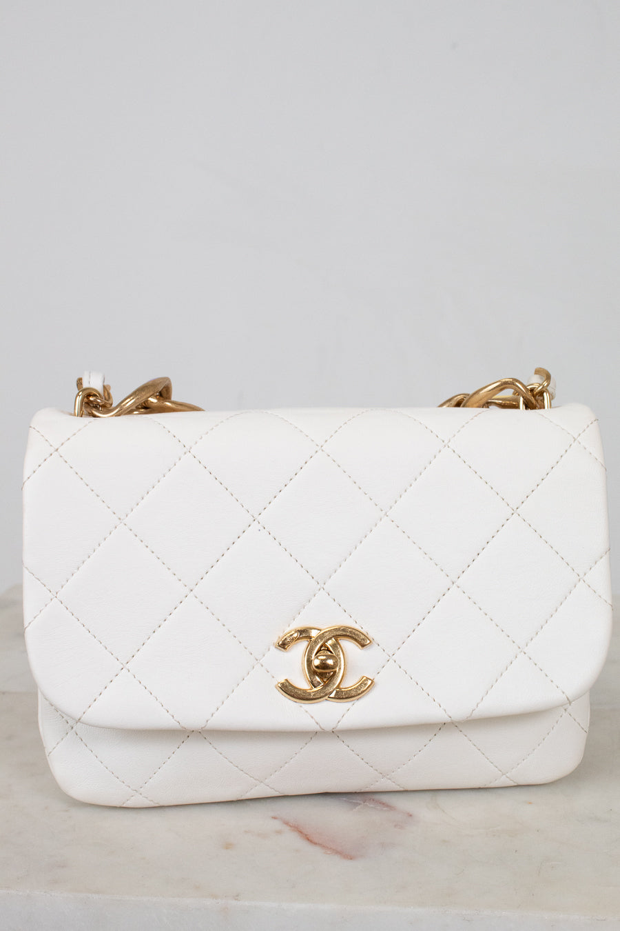 White quilted handbag with gold hardware on a light gray background