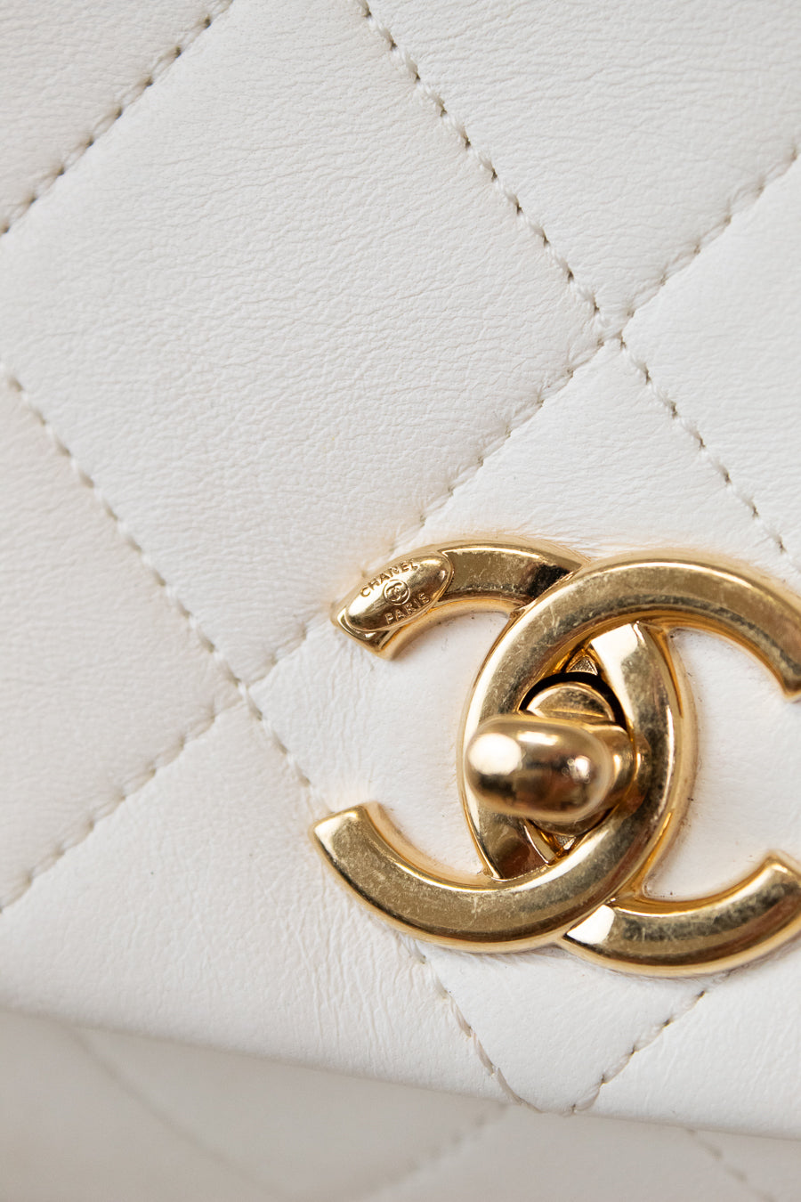 Close-up of a gold Chanel logo on a white quilted leather background