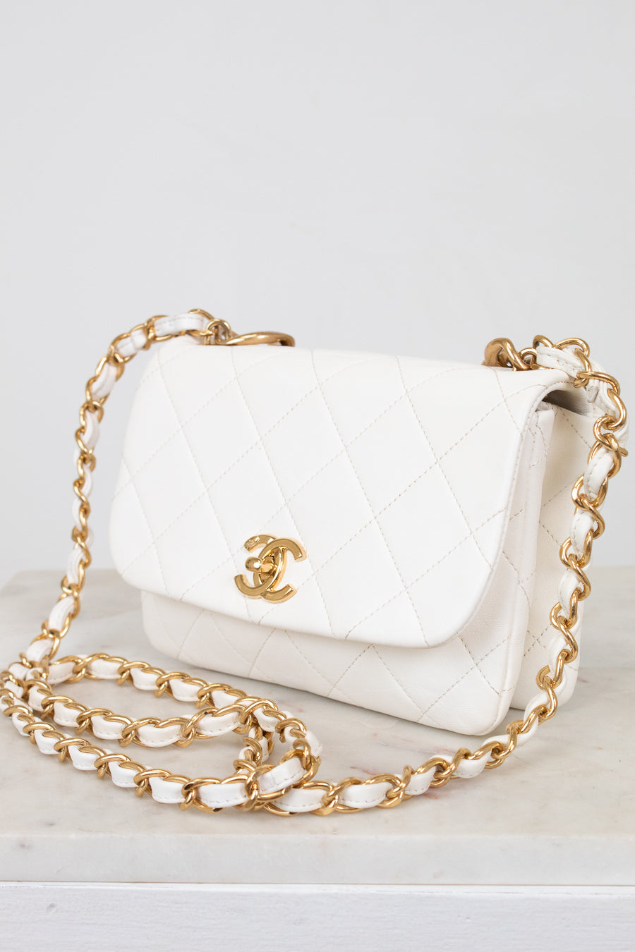 White handbag with gold chain and logo on a white background