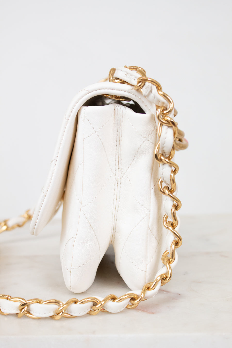 Side view of white quilted purse with gold chain strap on a light background