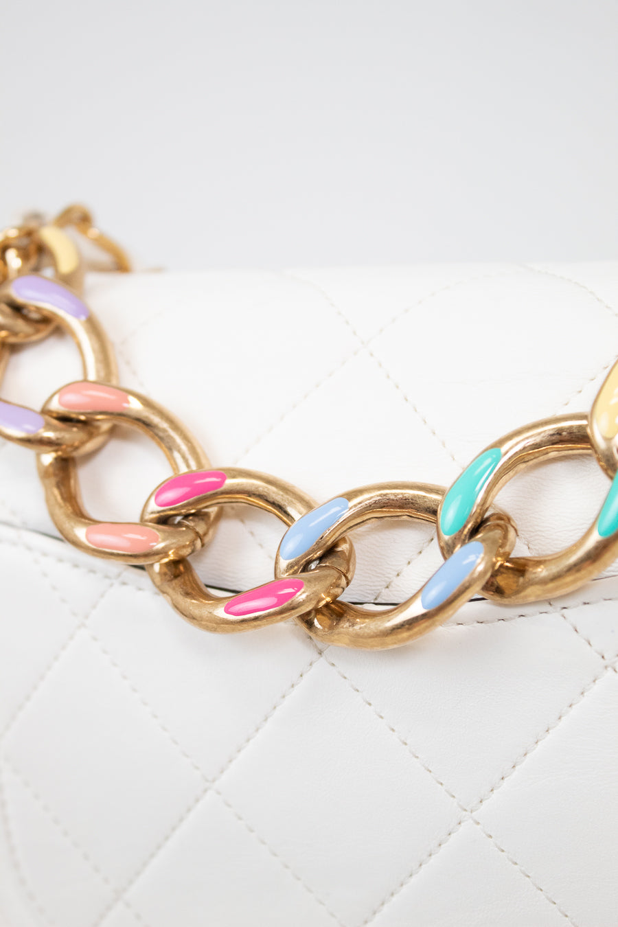 Gold chain bracelet with colorful links on a white quilted surface