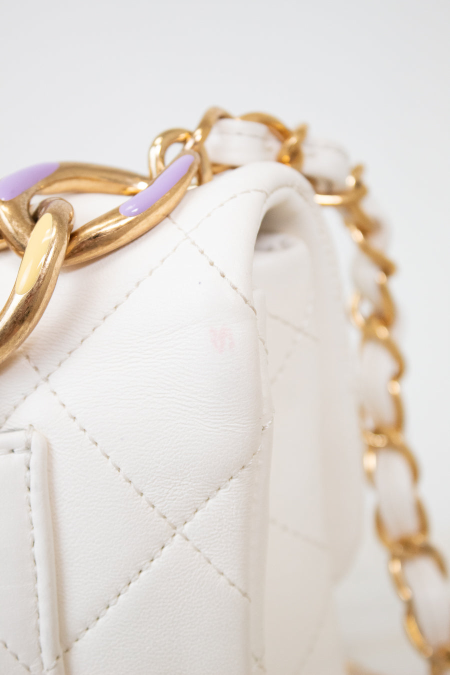 Close-up of a white quilted handbag with gold chain handle on a light gray background