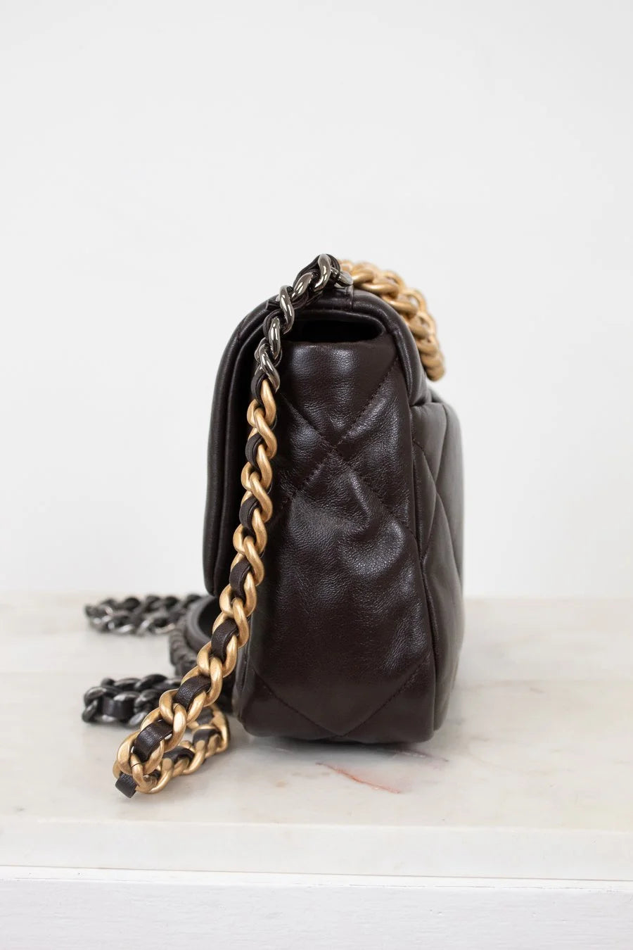 Brown leather handbag with gold chain strap on a white background