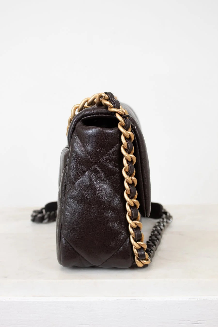 Brown quilted handbag with gold chain strap on a white background