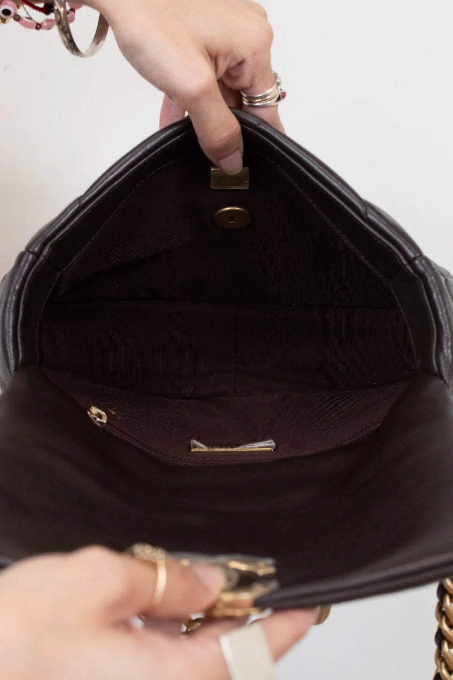 Close-up of a hand holding a dark brown handbag with gold accents.