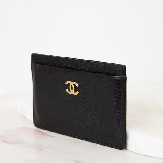 Black leather cardholder with gold logo on a white background