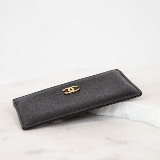 Black wallet with gold logo on a light marble surface