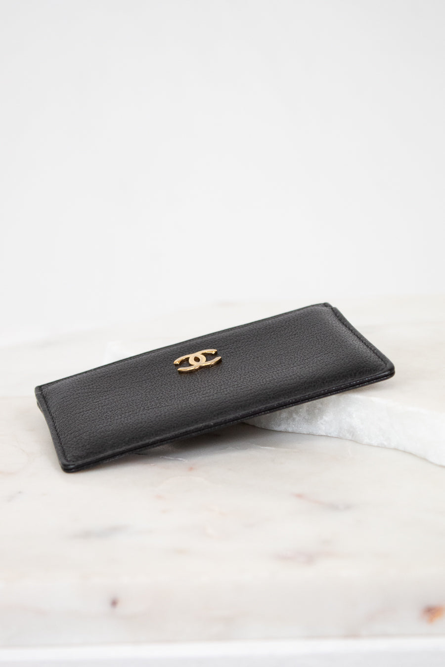 Black wallet with gold logo on a light marble surface
