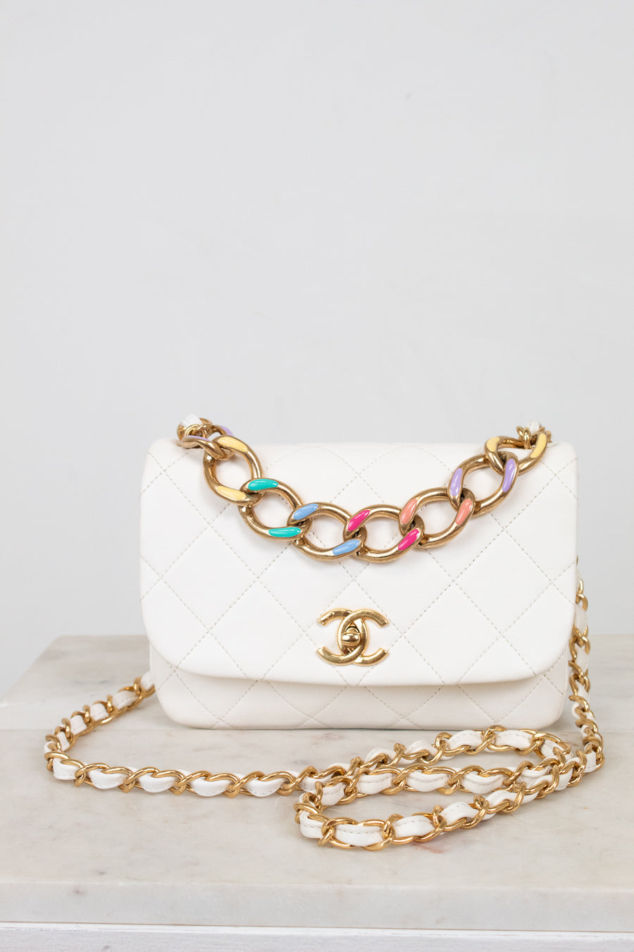 White Chanel handbag with gold chain on a light gray background