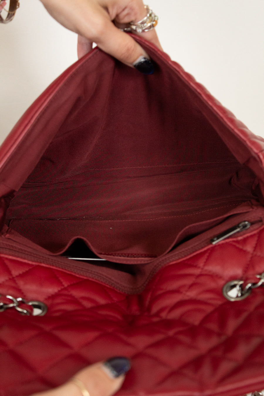 Red quilted handbag with a hand holding it open, showing the interior.