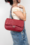 Person holding a red quilted handbag with a visible brand logo against a plain background