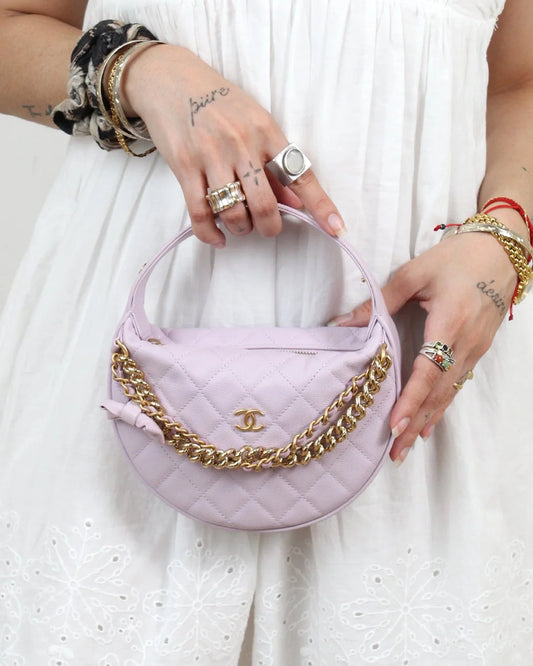 Person holding a lavender handbag with gold chain detail, wearing multiple rings and bracelets.
