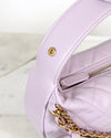 Close-up of a light pink/purple handbag with gold chain detail on a white background