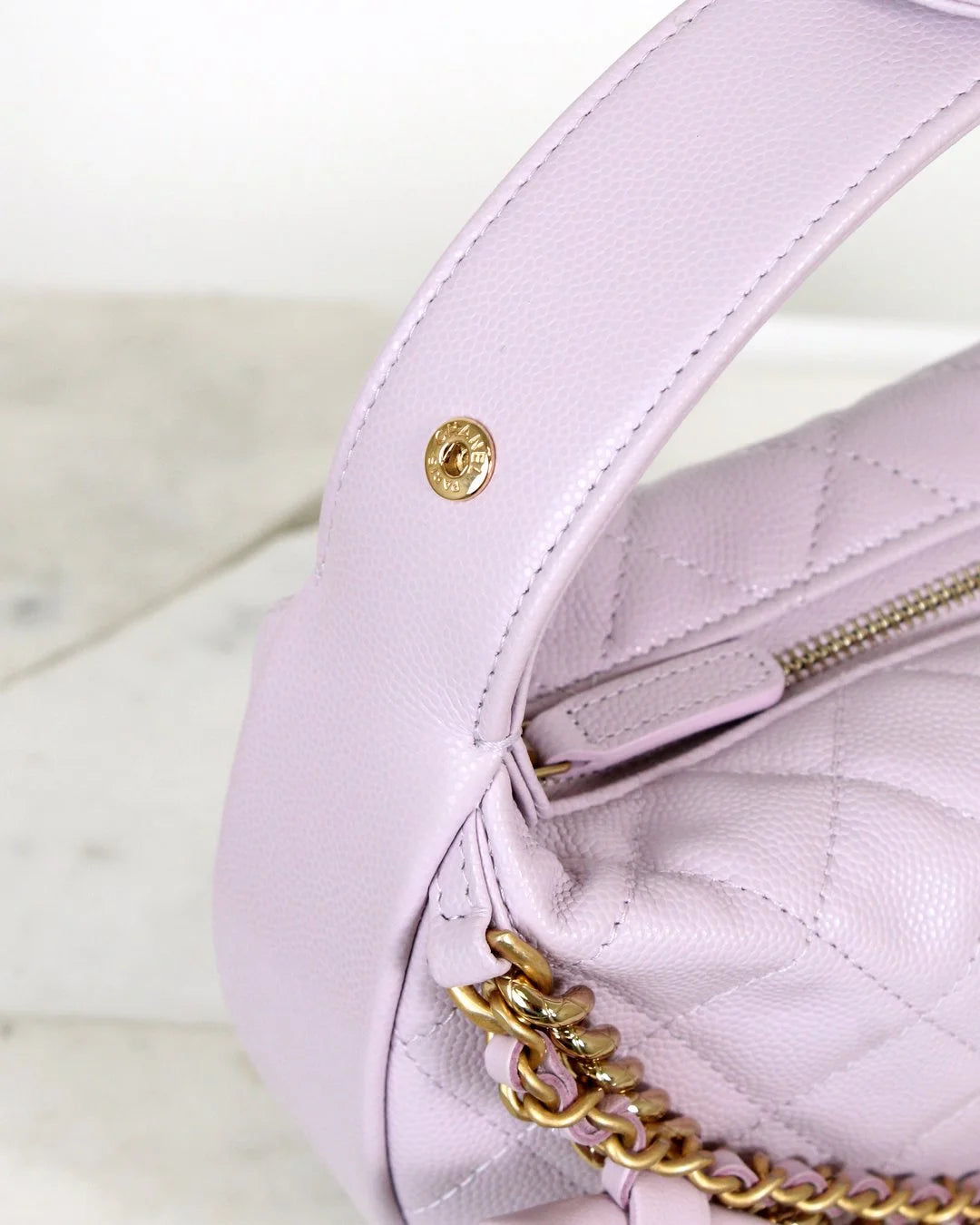 Close-up of a light pink/purple handbag with gold chain detail on a white background