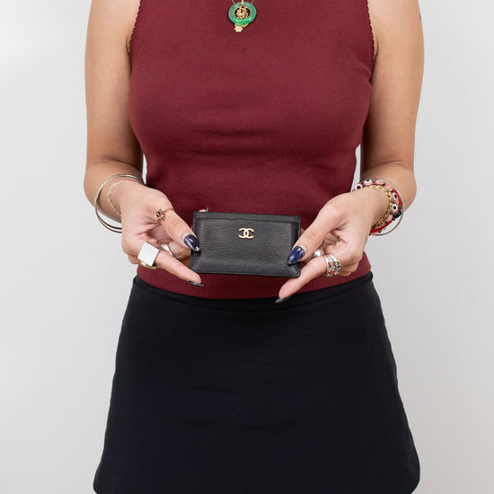 Person wearing a burgundy top and black skirt holding a small black handbag against a plain background