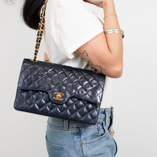 Person holding a navy quilted handbag with a gold chain strap against a plain background