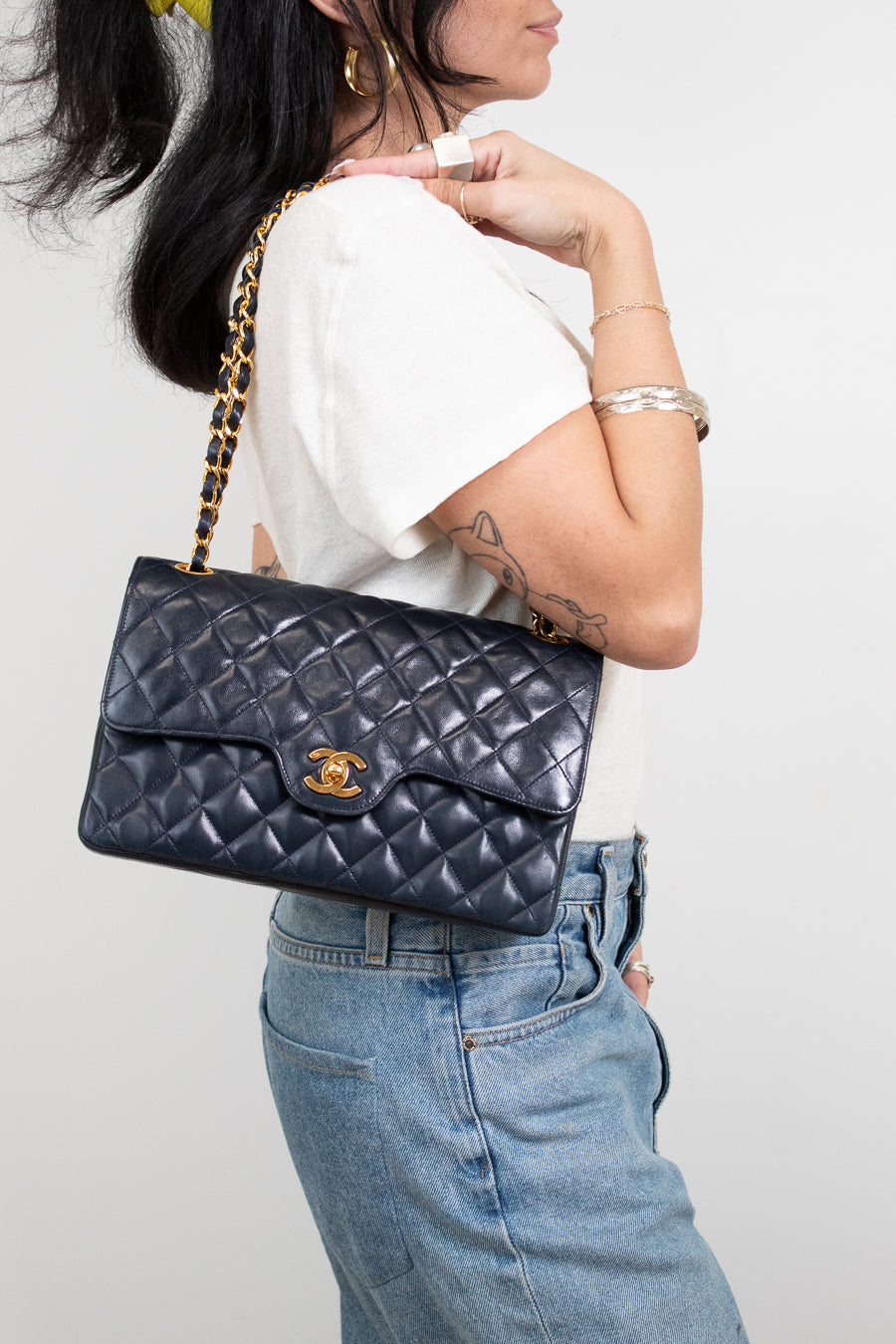 Person holding a navy quilted handbag with a gold chain strap against a plain background