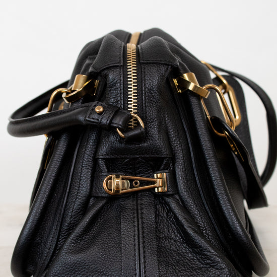 Black leather handbag with gold hardware on a white background