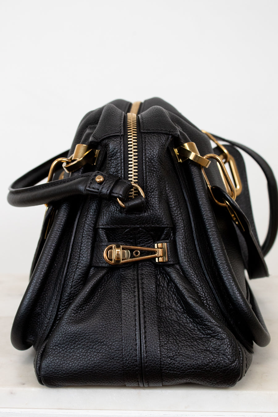 Black leather handbag with gold hardware on a white background