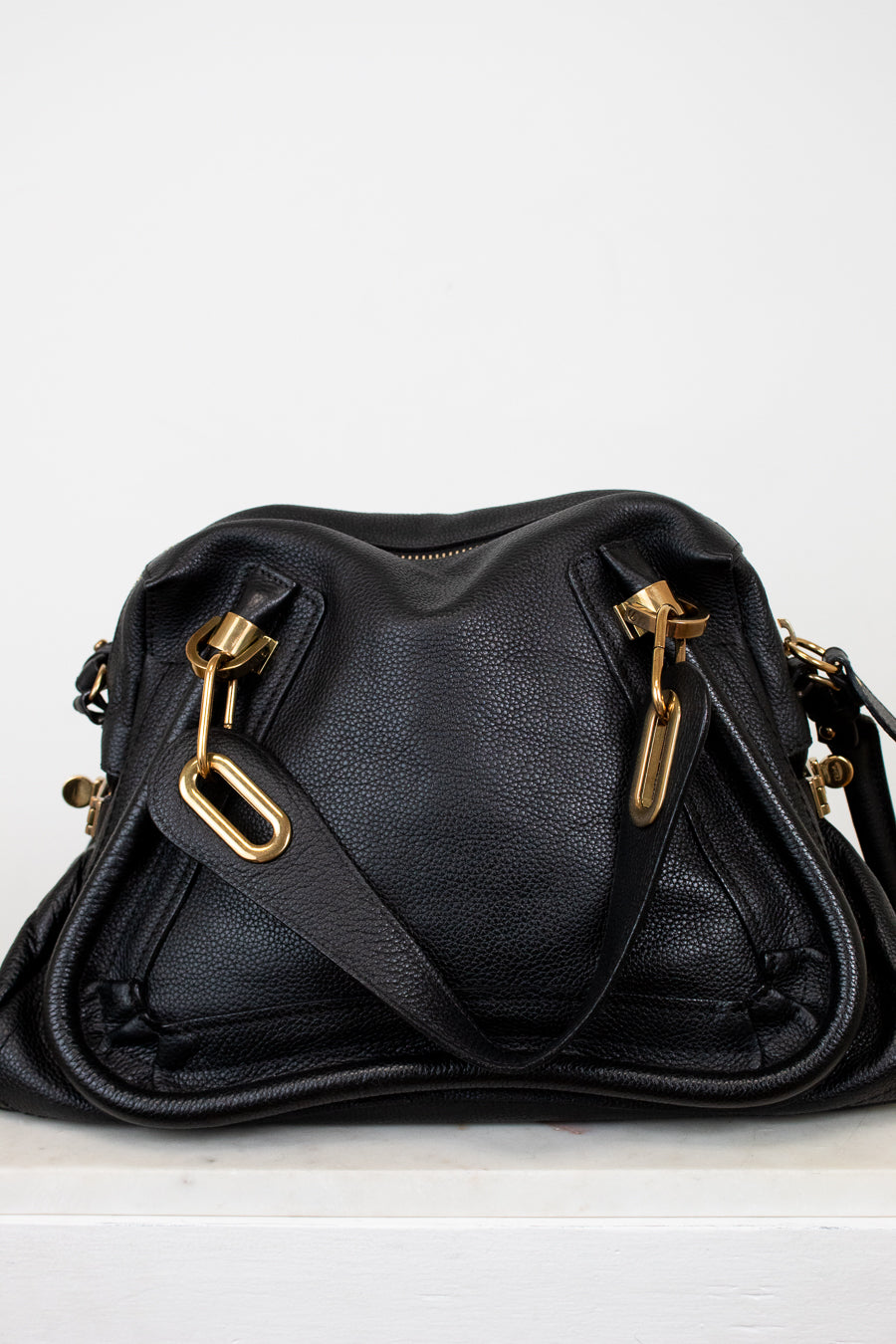 Black leather handbag with gold hardware on a white background