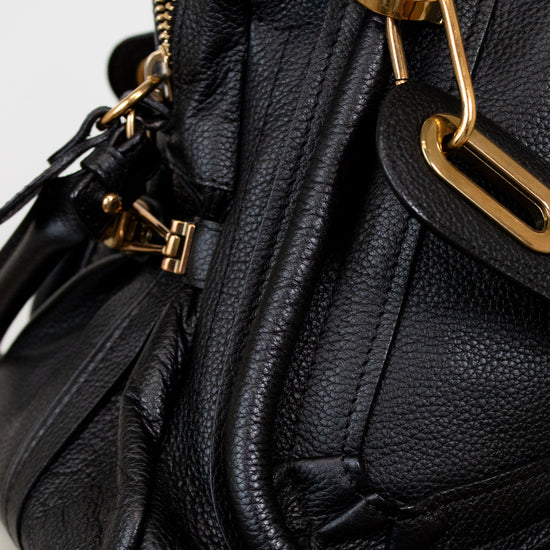 Black leather handbag with gold hardware on a light gray background