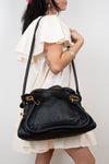 Person holding a black handbag against a plain background