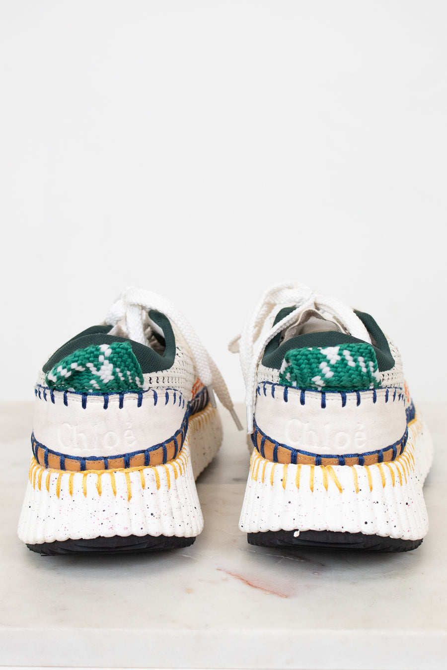 Pair of white sneakers with green and blue accents on a light background