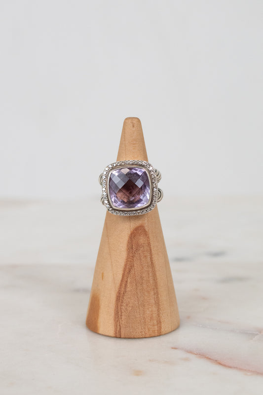 Ring with a purple gemstone on a wooden stand against a light background