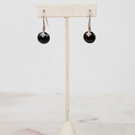 Black earrings on a beige stand against a white background