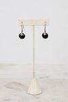 Black earrings on a beige stand against a white background