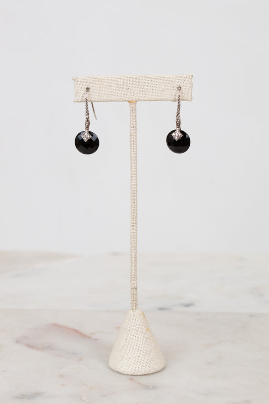 Black earrings on a beige stand against a white background