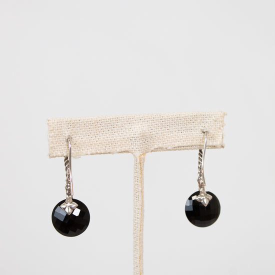 Black earrings on a beige earring stand against a white background